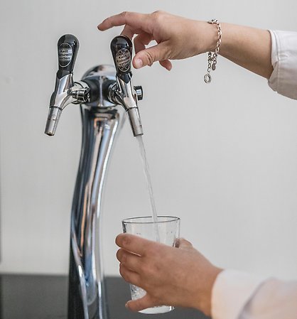 En hand som fyller på ett glas vatten vid en vattenkran.